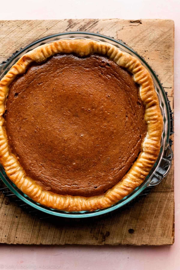 pumpkin pie on wooden cutting board set on a pink backdrop.