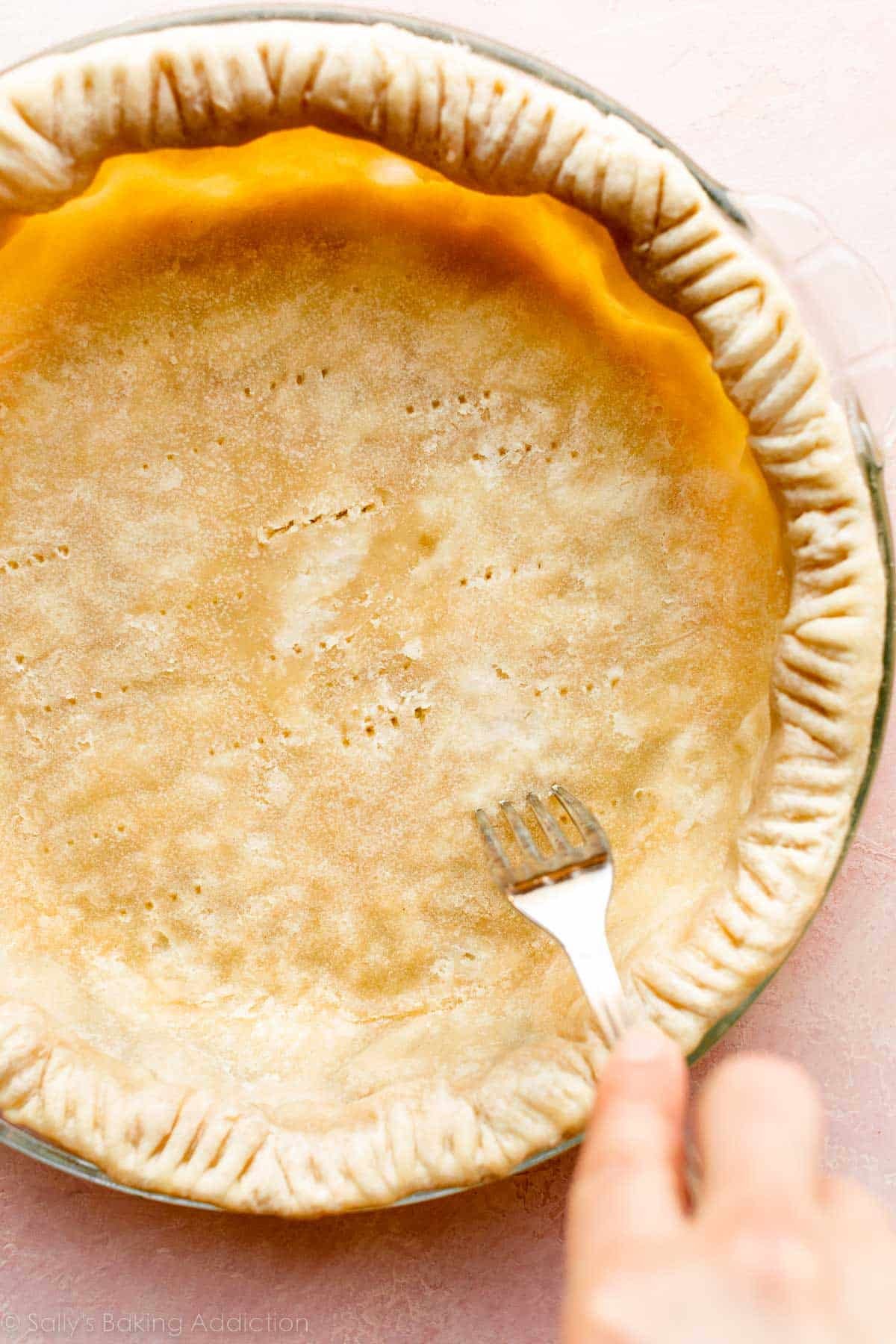 pricking the bottom of par-baked pie crust with fork.