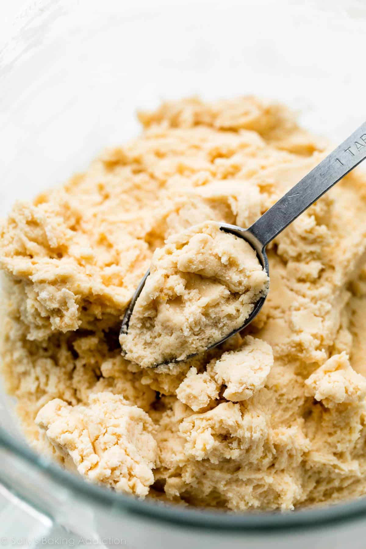 Tablespoon measuring spoon measuring cookie dough in glass bowl.