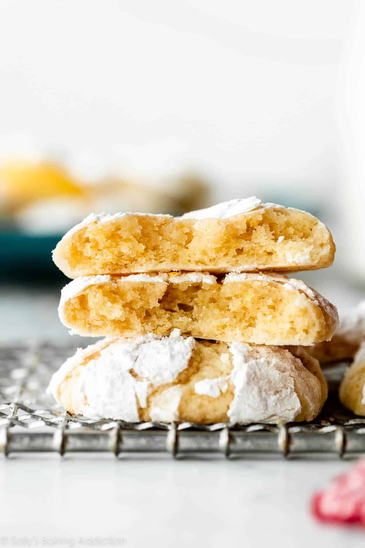 stack of lemon crinkle cookies with one cookie broken in half.