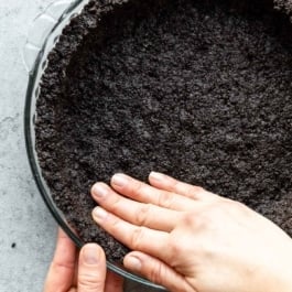 two hands pressing Oreo cookie crust into pie dish.