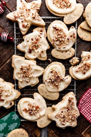 small wire rack with brown butter frosted pecan cookies on top in the shapes of stars, mittens, and trees.