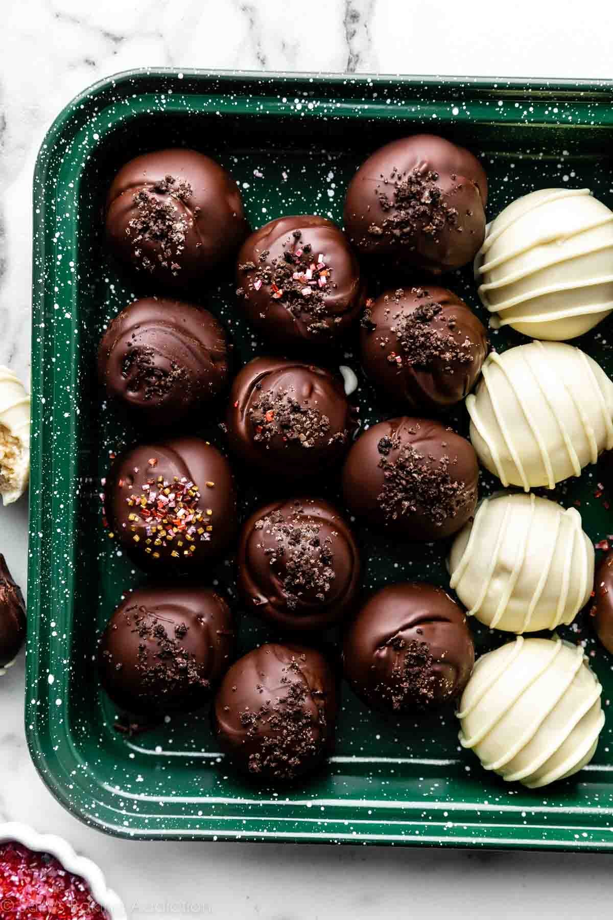 chocolate coated and white chocolate coated oreo truffles on green baking sheet.