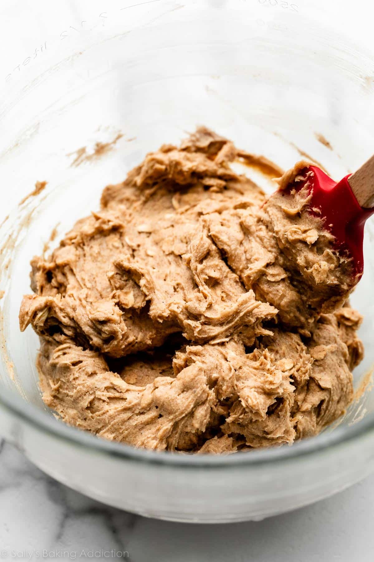 brown sugar oatmeal cookie dough in glass bowl with red spatula.