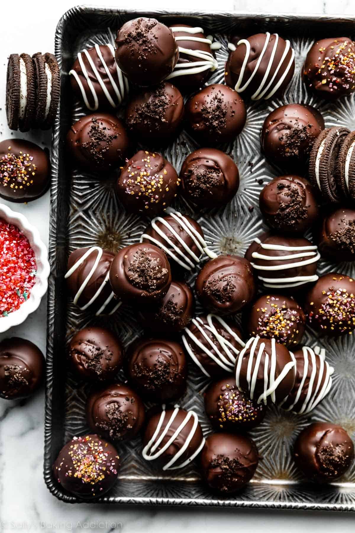 chocolate coated and white chocolate coated and drizzled oreo truffle balls on silver baking sheet.