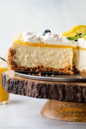 removing a slice of lemon cheesecake with lemon curd and whipped cream from base of springform pan.