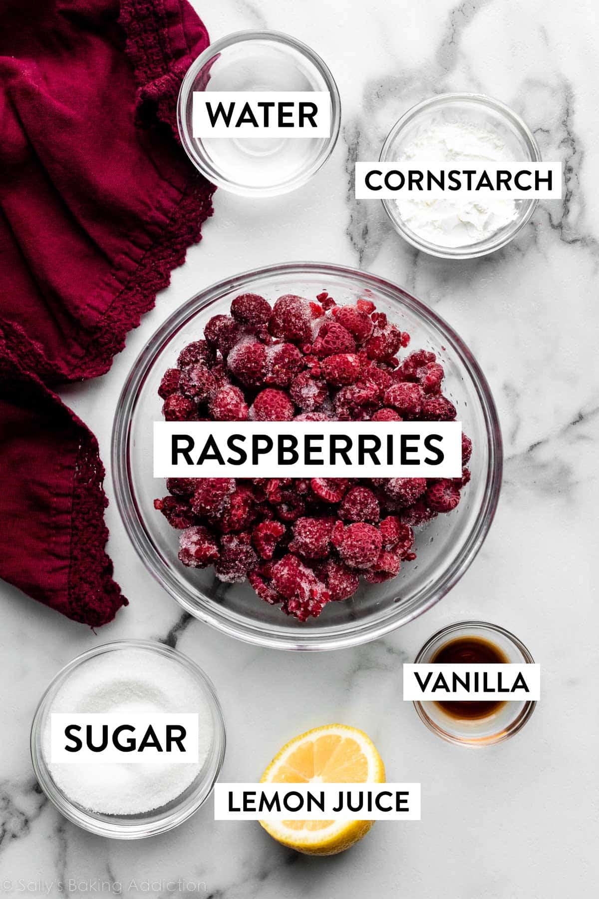 bowls of ingredients on marble counter including frozen raspberries, water, cornstarch, vanilla, and sugar with half of a lemon next to it.