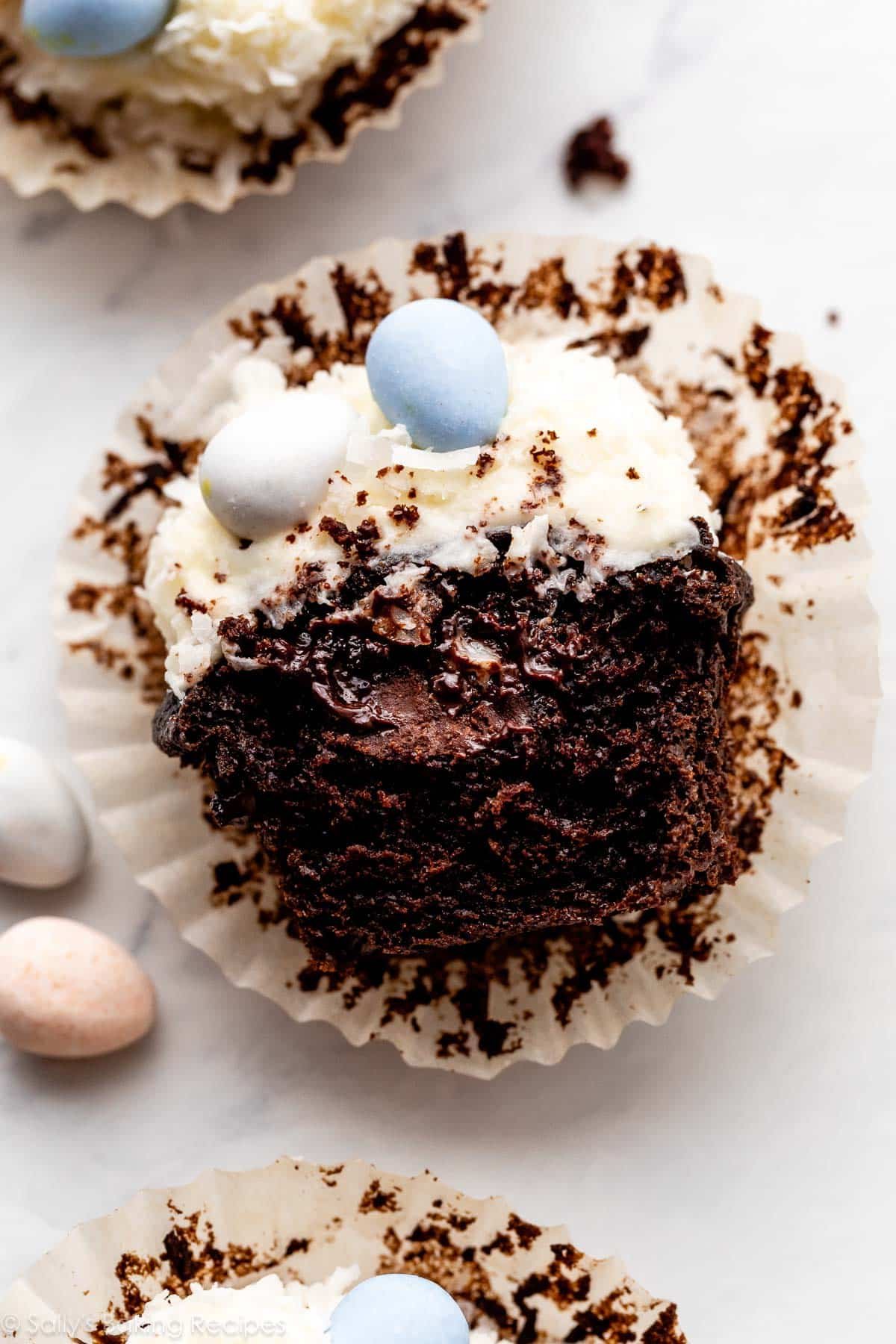 chocolate cupcake split in half to show ganache center and coconut cream cheese frosting on top.