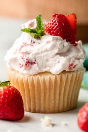 close-up of strawberry shortcake cupcake with whipped cream, mint, and fresh strawberry slices on top.