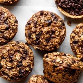 chocolate chip baked oatmeal cups on gray backdrop with wooden bowl of mini chocolate chips.