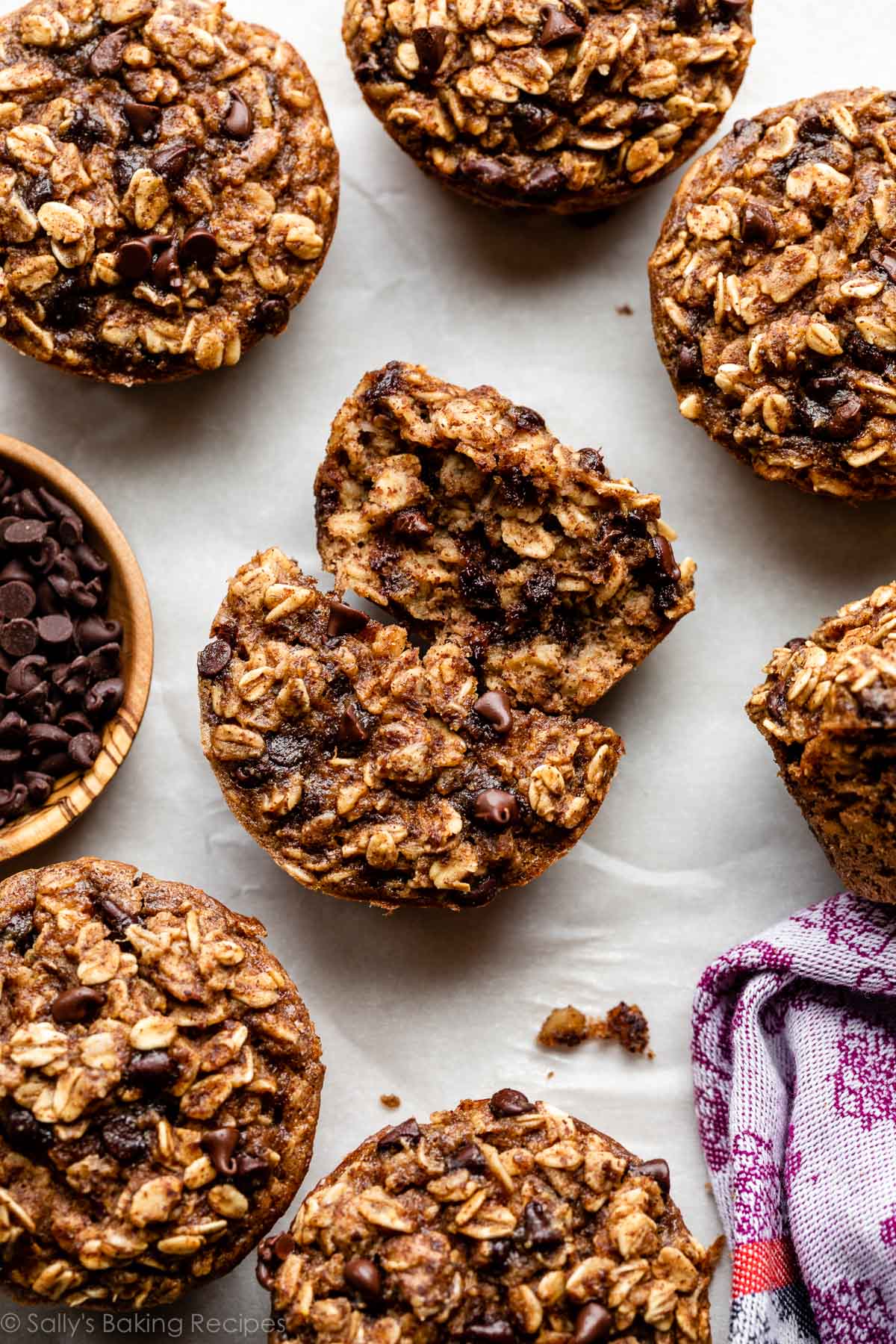 chocolate chip baked oatmeal cup muffins on white parchment paper with one in center broken open.