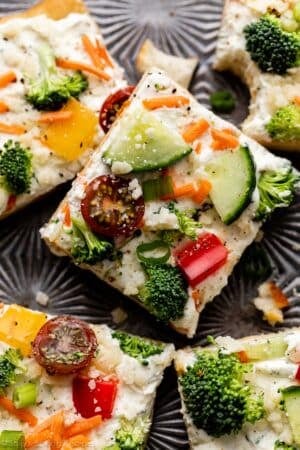 veggie pizza with fresh broccoli, red pepper, cucumber, cherry tomatoes, parmesan cheese, and scallion on top.