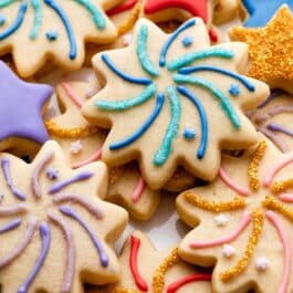 sugar cookies decorated like fireworks and stars with blue, red, pink, and purple icing with shimmery sprinkles on top.