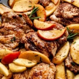 close up photo of apple cider chicken with apples and rosemary in skillet.