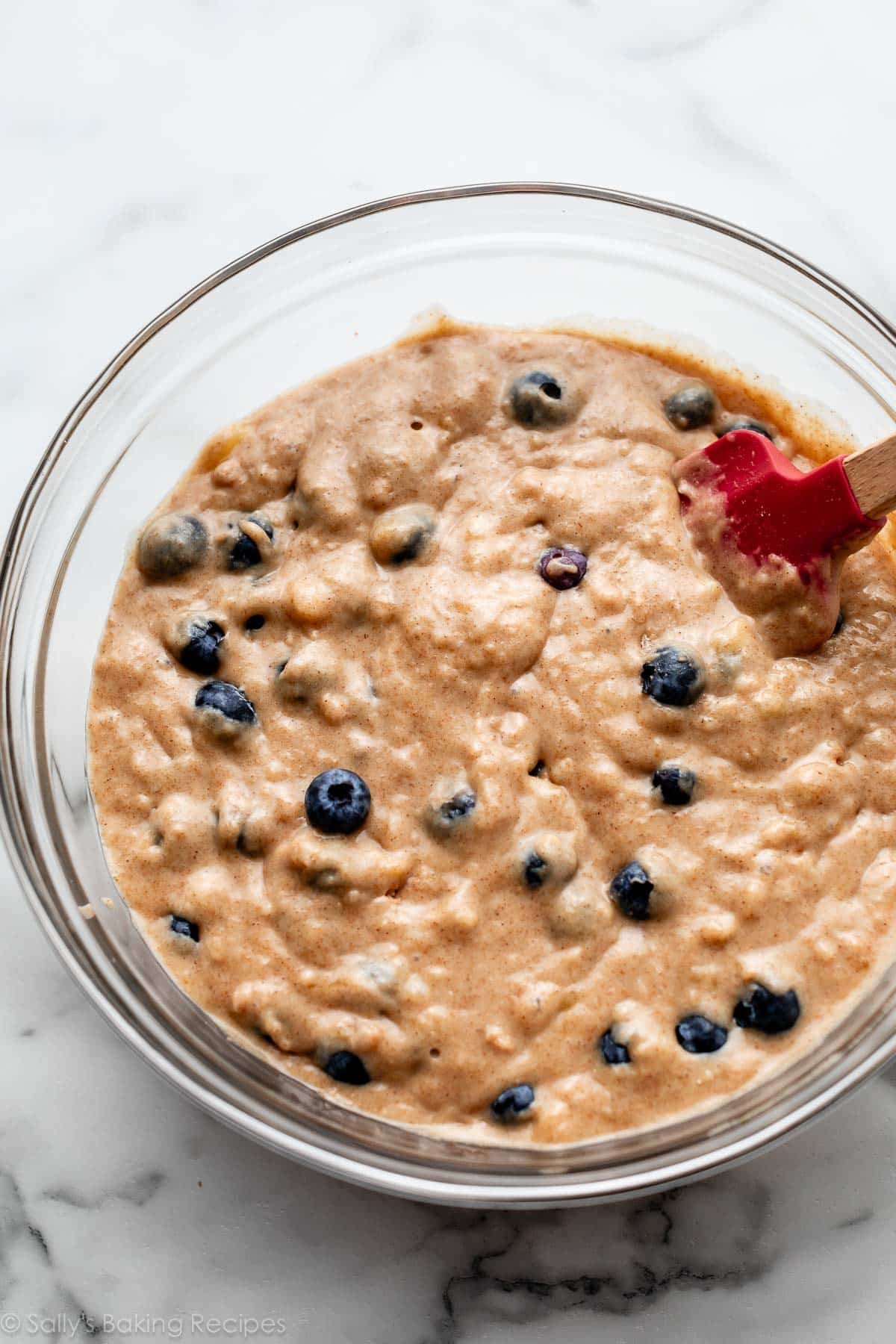 muffin batter with blueberries in glass bowl on marble counter.