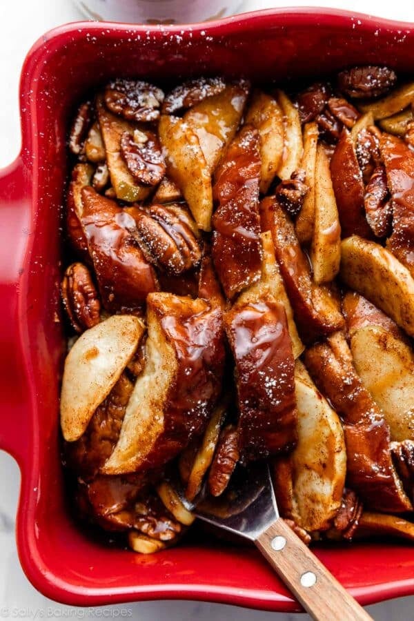 removing a serving of apple french toast out of red casserole dish.