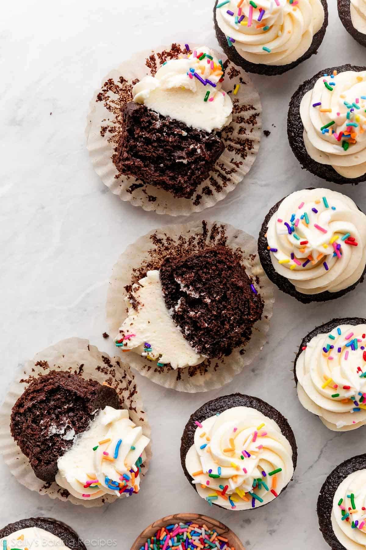 chocolate cupcakes with vanilla buttercream on marble counter with a couple cut in half.