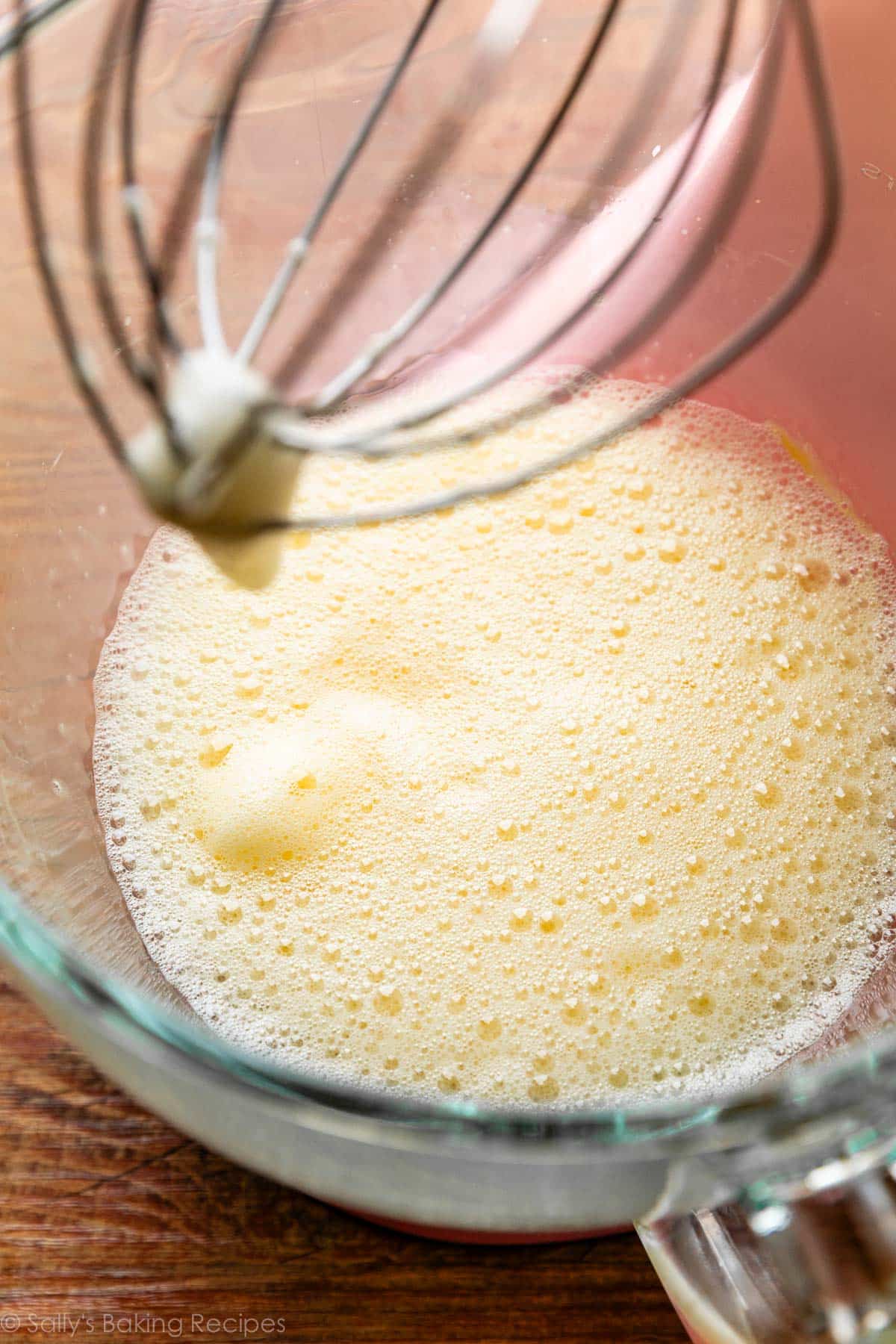 whipped eggs with bubbles on surface in glass bowl on wooden surface.