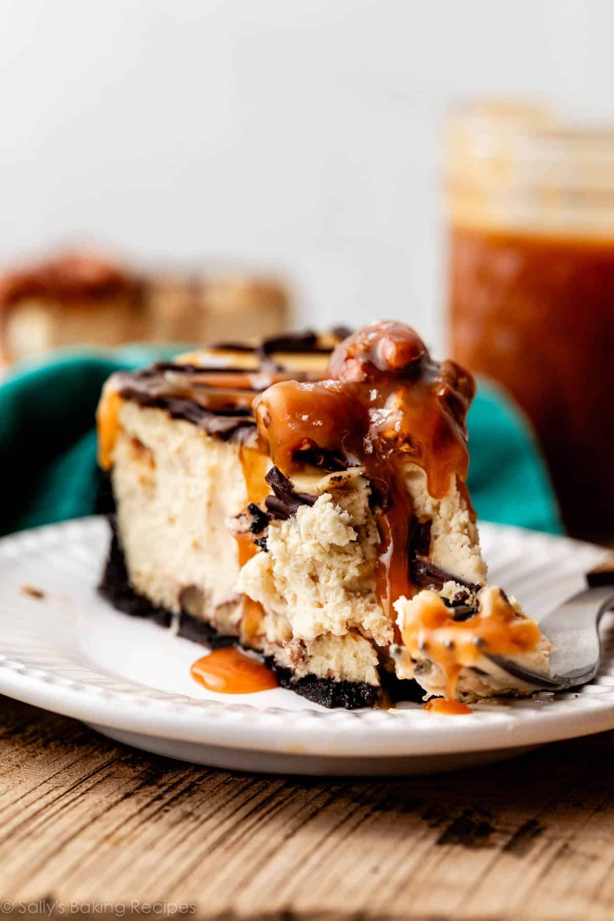 slice of caramel chocolate pecan cheesecake on white plate with fork.