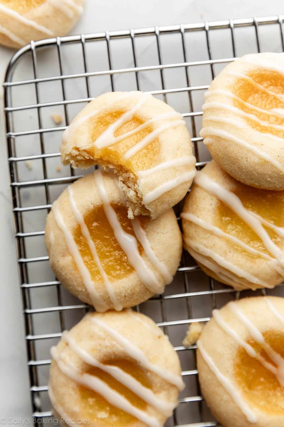 close-up overhead photo of lemon thumbprint with bite taken out with other whole cookies on cooling rack.