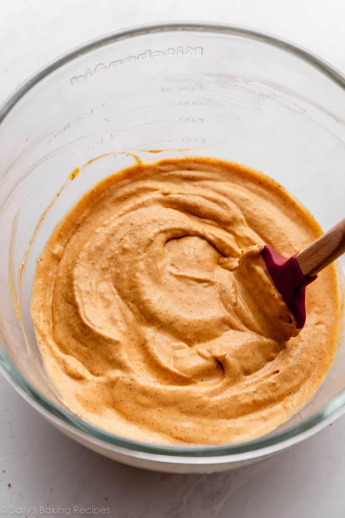 pumpkin batter in glass bowl with red spatula.