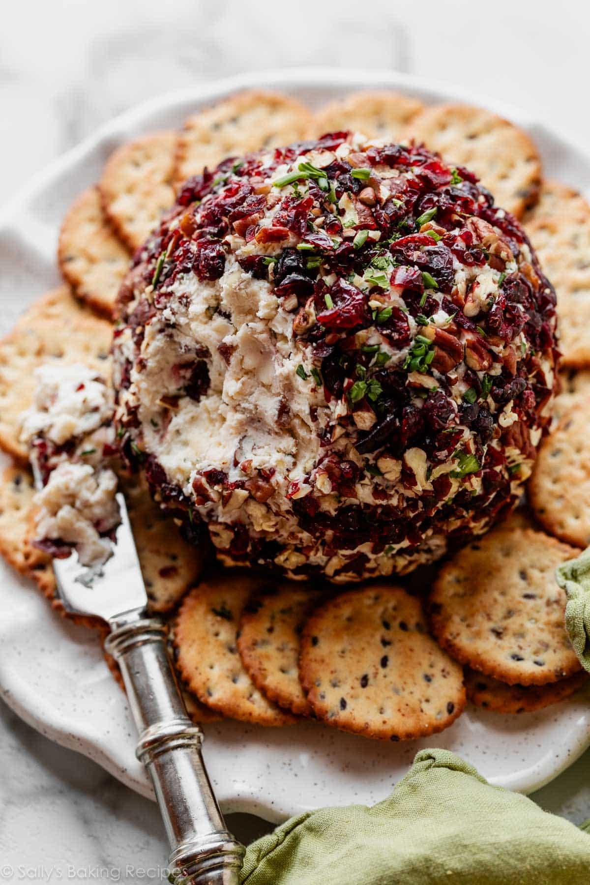 cranberry white cheddar cheese ball cut open with crackers on plate.