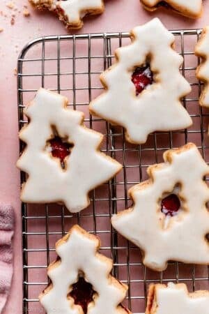 Christmas-tree shaped cherry almond linzer cookies with icing on cooling rack.