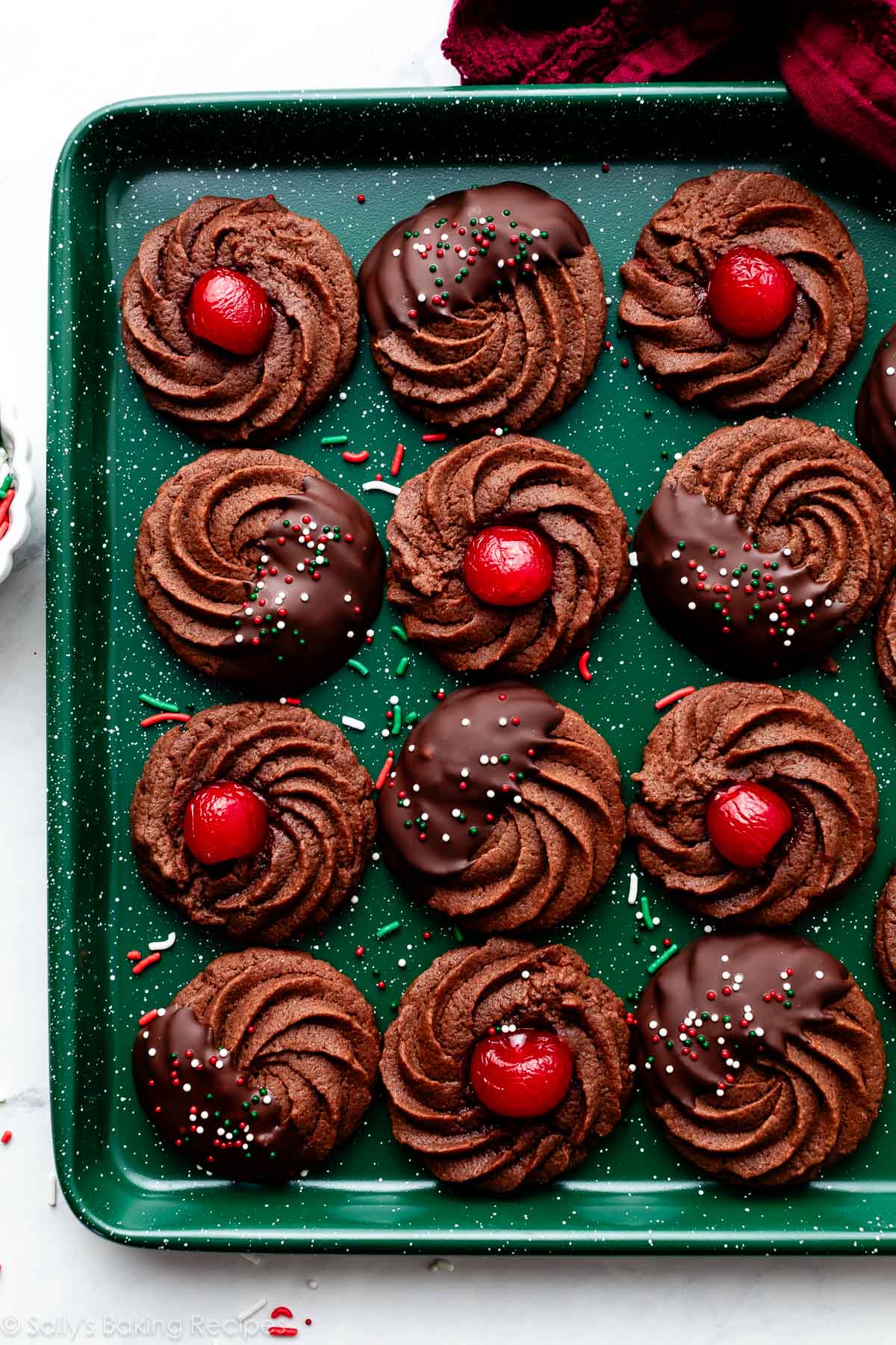 chocolate butter cookies with chocolate and cherries on green baking sheet.