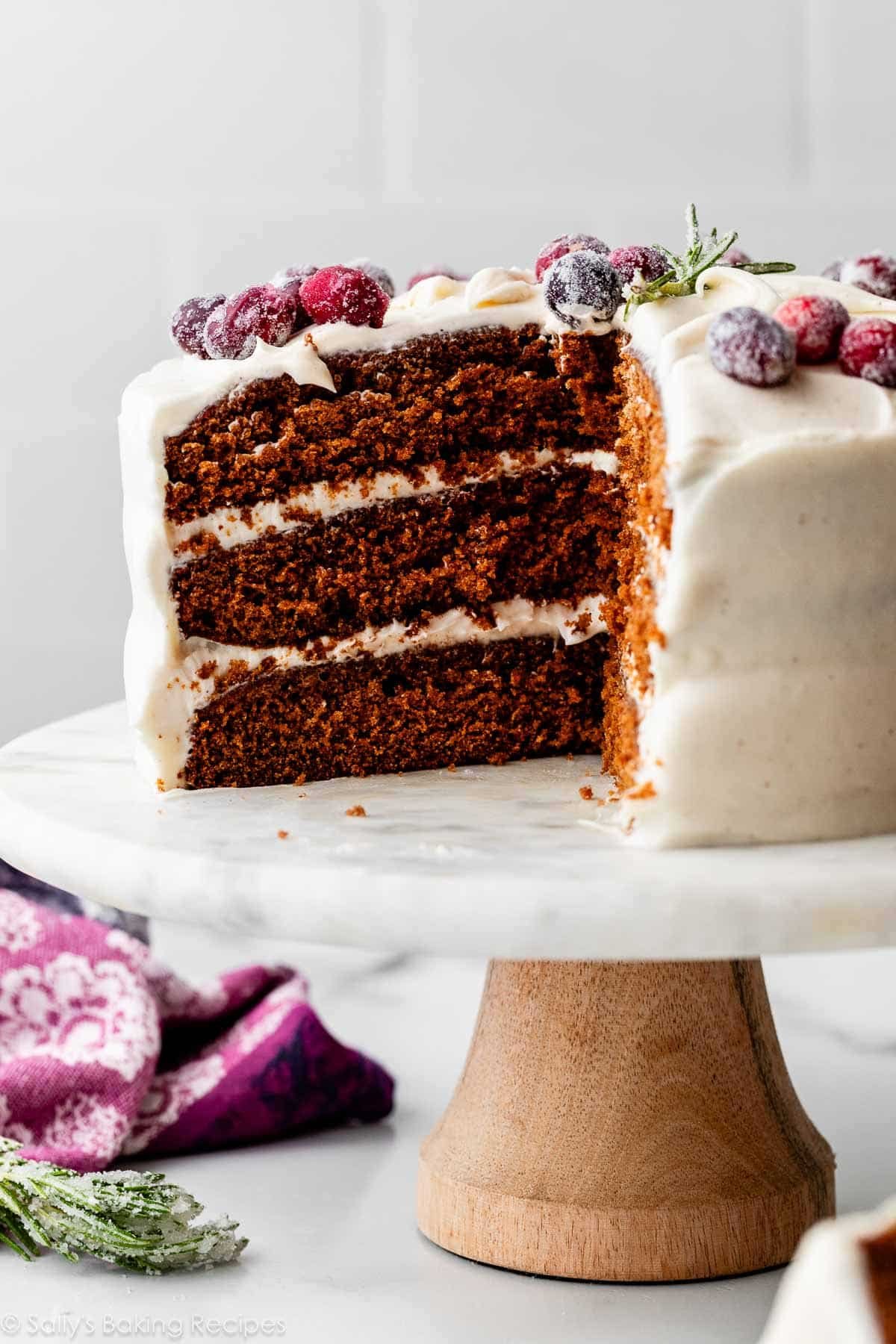 3 layer gingerbread cake with cream cheese frosting and sugared cranberries on top.