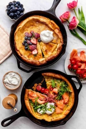 two dutch baby pancakes pictured in cast iron skillets, with one with berries and whipped cream and the other with smoked salmon and arugula.