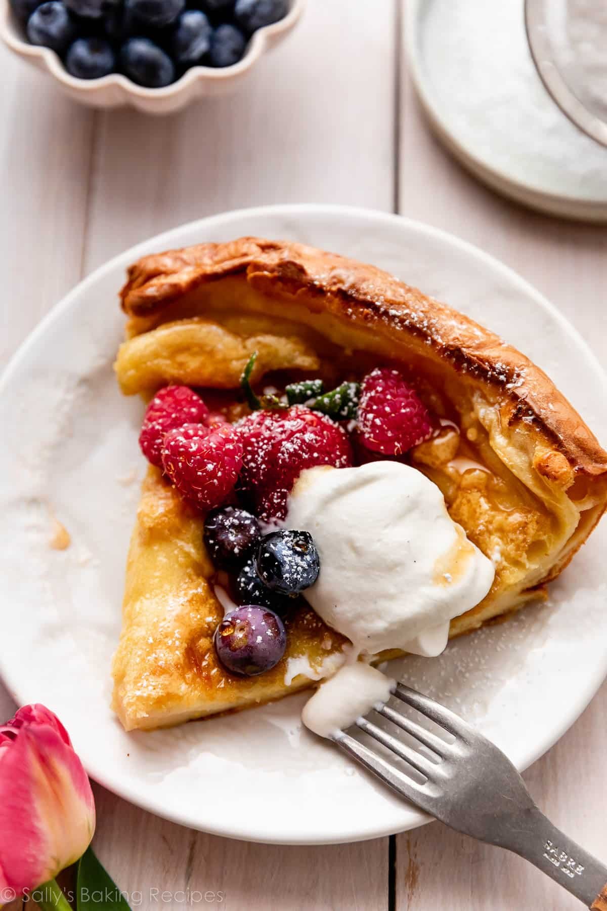 dutch baby pancake slice on plate with berries and whipped cream.