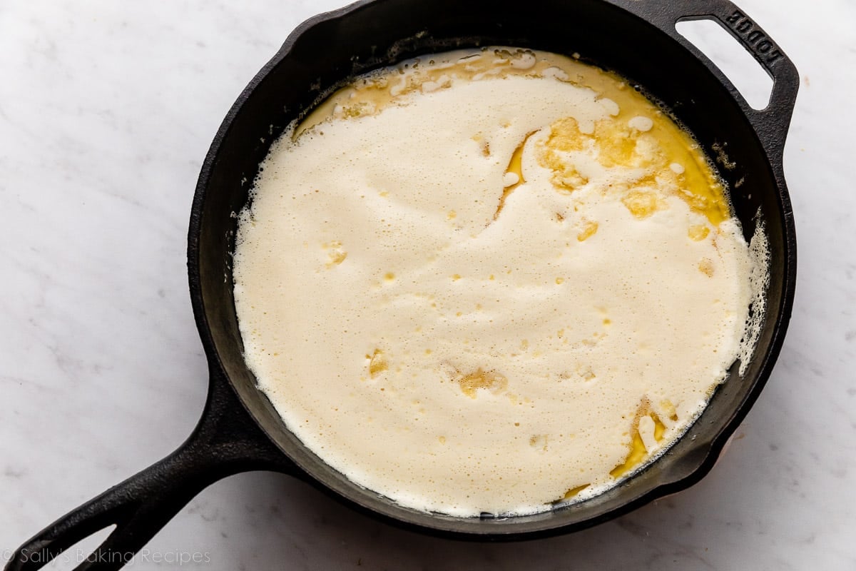 cast iron skillet pictured with batter and melted butter inside.