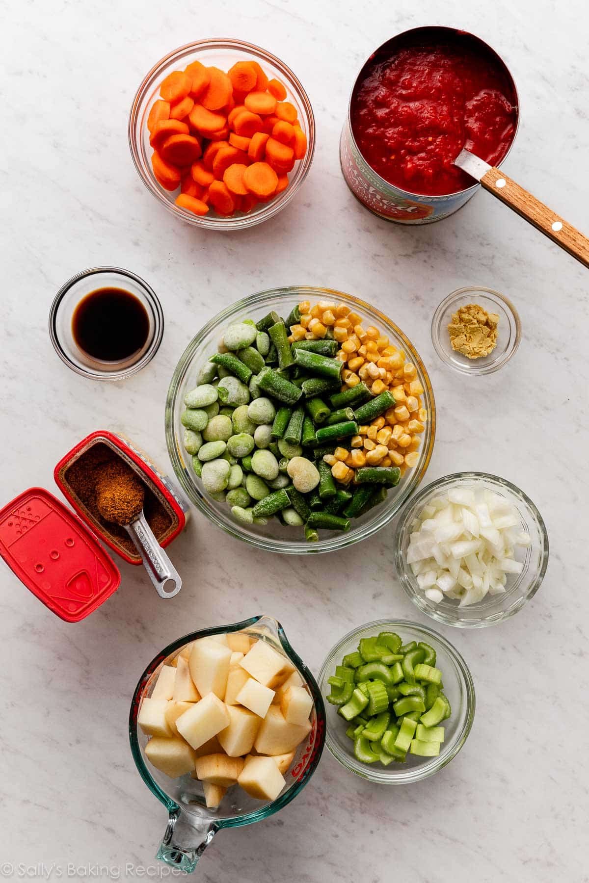 ingredients on marble counter including frozen vegetables, Old Bay Seasoning, potatoes, onions, and crushed tomatoes.