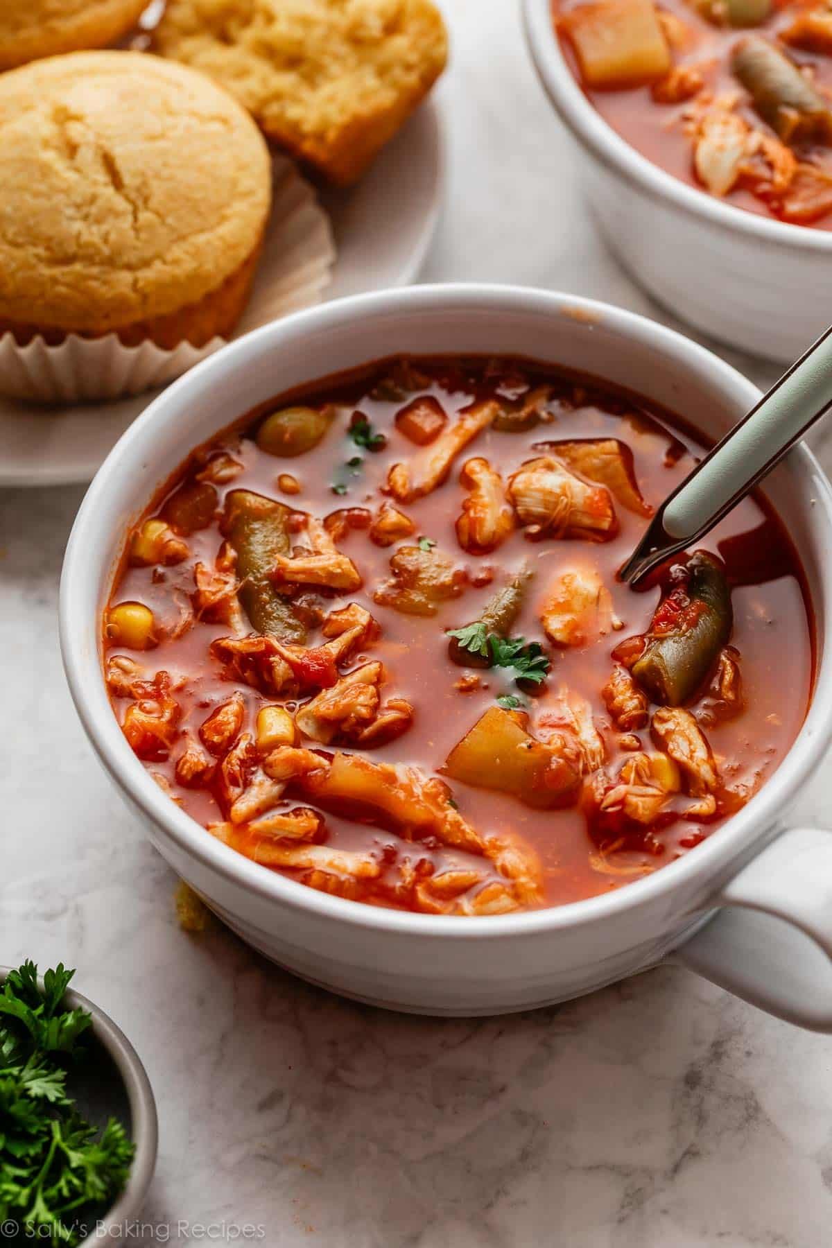 white mug of Maryland crab soup with cornbread muffins in the background.