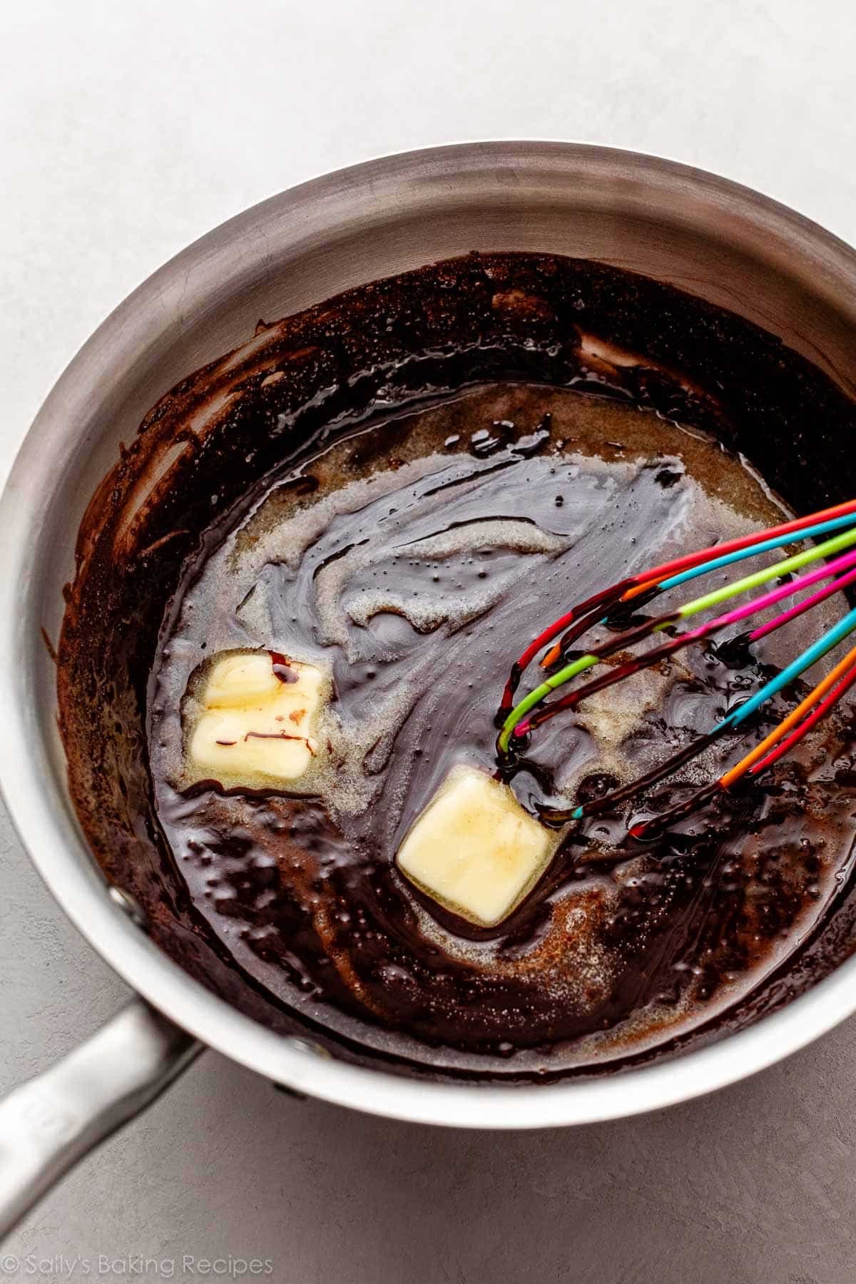 chocolate sauce in pot with two pieces of butter being whisked in.