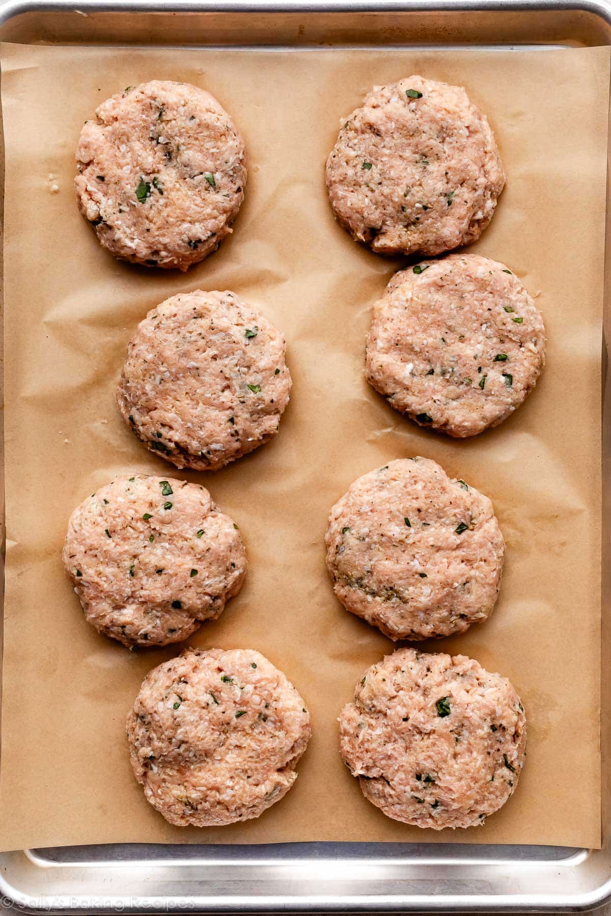 shaped chicken burgers on lined baking sheet.