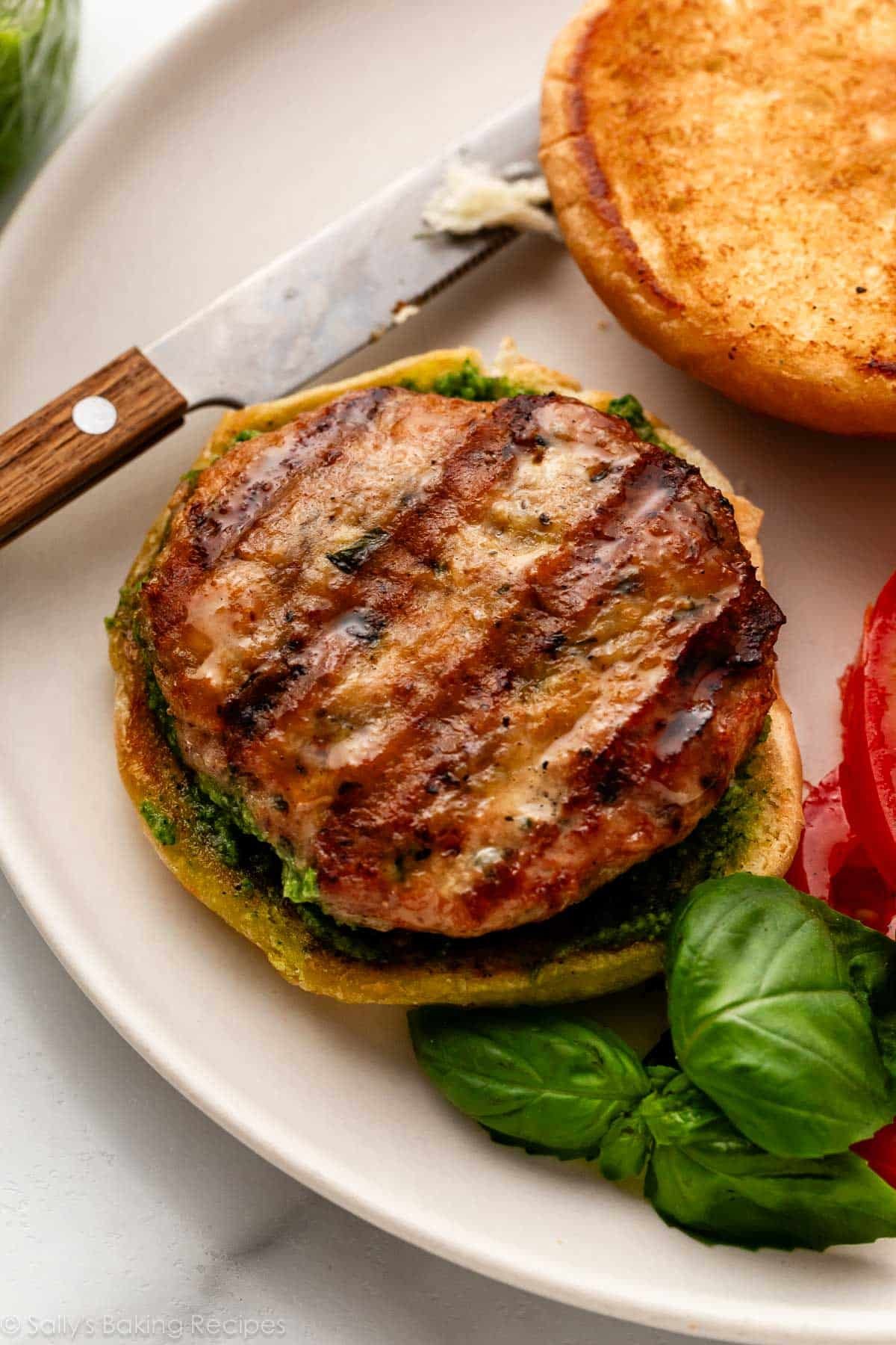 chicken burger on bun with fresh basil next to it.