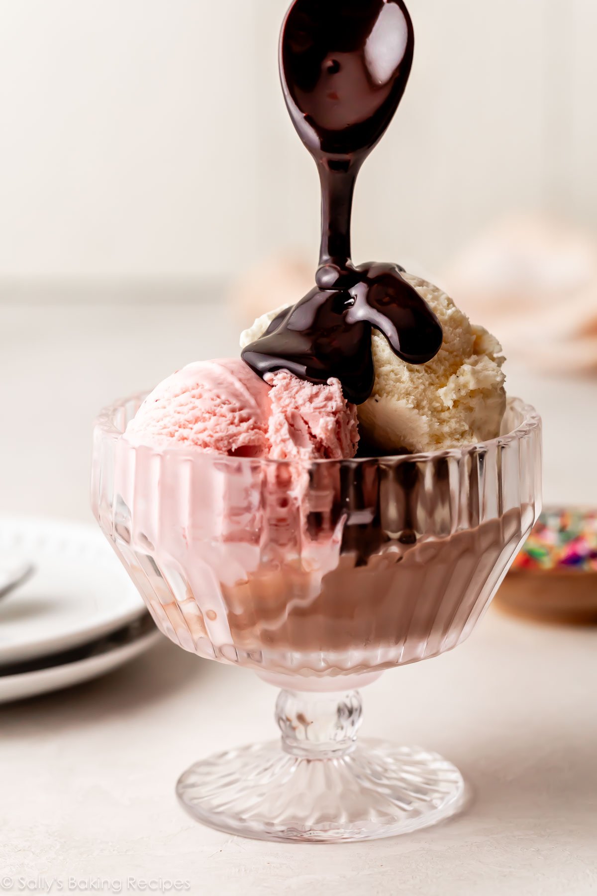 hot fudge being spooned on top of bowl of strawberry and vanilla ice cream.