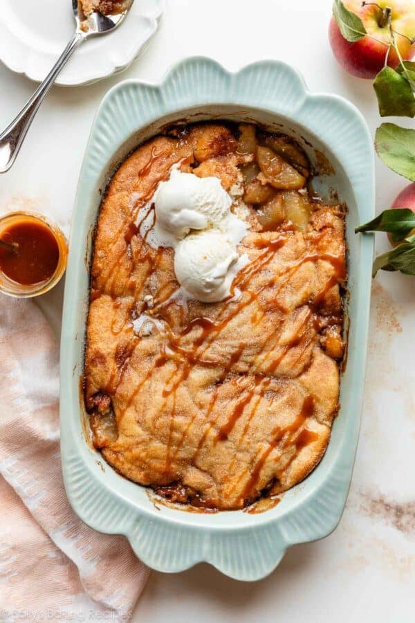 apple cobbler in a blue baking dish with caramel and cinnamon, topped with vanilla ice cream.