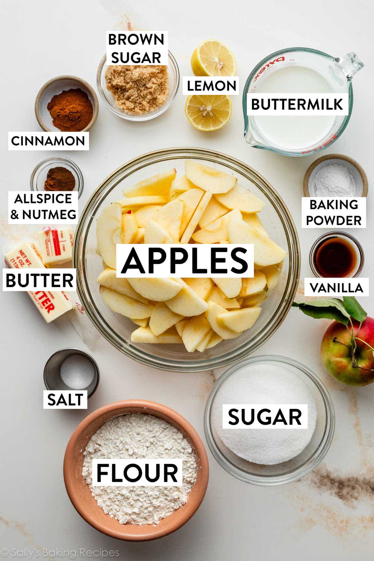 ingredients on marble counter including buttermilk, baking powder, salt, vanilla, flour, sugar, butter, and spices.