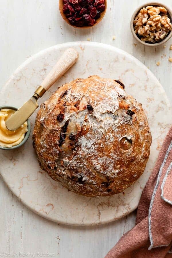 round boule loaf of cranberry nut bread with honey butter on marble serving tray.