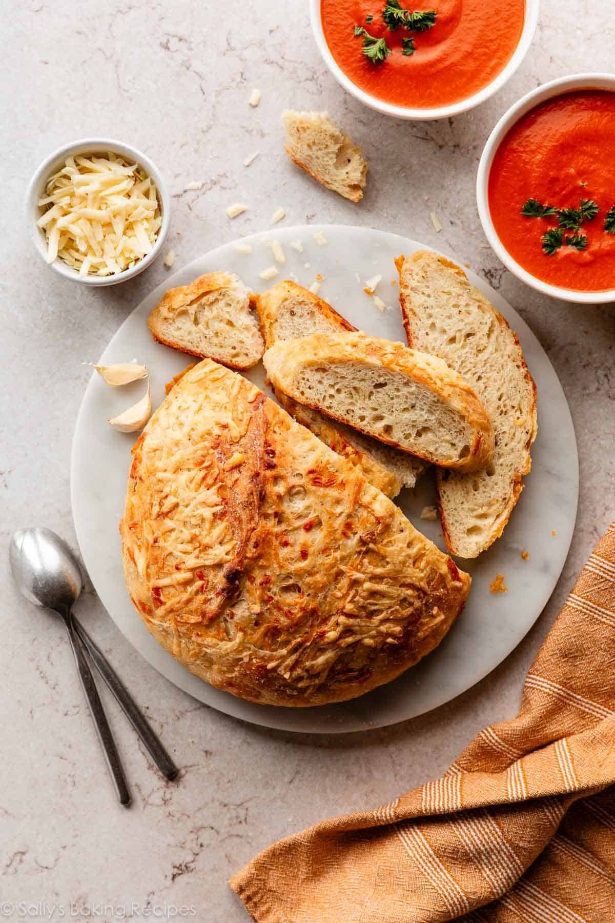 asiago cheese-crusted bread on marble cutting board with 2 bowls of tomato soup.