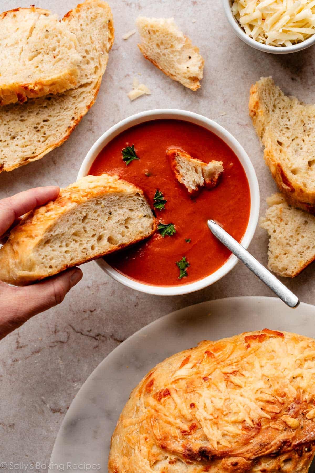 dipping a slice of asiago bread into a bowl of tomato soup.